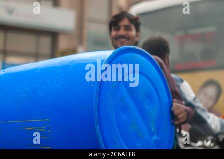 An Indian man riding pillion backwards while carrying a drum. This is an example of 'jugaad' or a non-conventional solution to carry a drum on a bike. Stock Photo