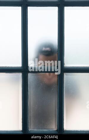 Boy looks through front door window Stock Photo