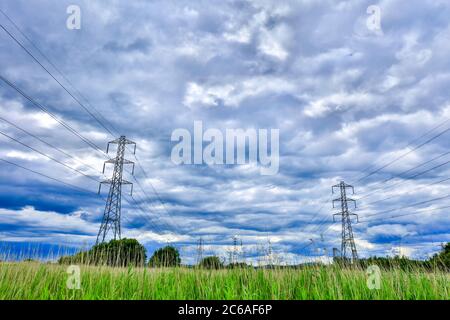 Electricity pylons part of the national grid with cables stretching into the distance against blue dramatic sky Stock Photo