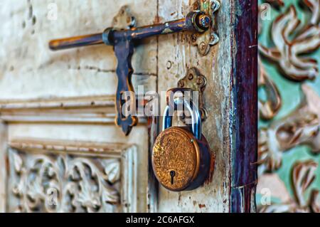 A brass padlock is suspended from a staple on a partially open door. An old fashioned and weather brass hasp is also visible in the image. Stock Photo