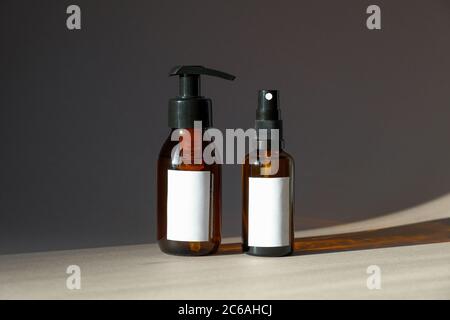 Amber glass cosmetic bottles mockups. Pump bottle with natural hand cream and spray bottle with body lotion. Cosmetic product packaging design Stock Photo