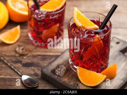 Negroni cocktail in crystal glasses with orange slice and fresh raw oranges on chopping board with strainer on wood background. Top view Stock Photo