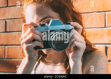 young woman holds an analog camera and looks through the viewfinder Stock Photo