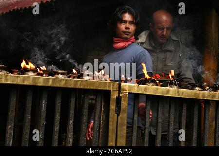 Ritual slaughter rests after animal sacrifices with blood on his hands next to ritual oil lamps in the main sanctuary in the Dakshinkali Temple near Kathmandu, Nepal. One of the major Hindu temples in Nepal dedicated to the goddess Kali is known for its animal sacrifices which take place in the main sanctuary. Stock Photo