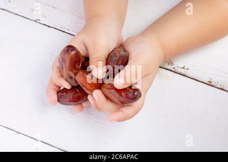 Many Dried date fruits in kids palms. Hands holding dates Stock Photo