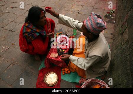 Brahmin applies a tilaka mark on the forehead of a woman next to the entrance to the Dakshinkali Temple near Kathmandu, Nepal. One of the major Hindu temples in Nepal dedicated to the goddess Kali is known for its animal sacrifices which take place in the main sanctuary. Stock Photo