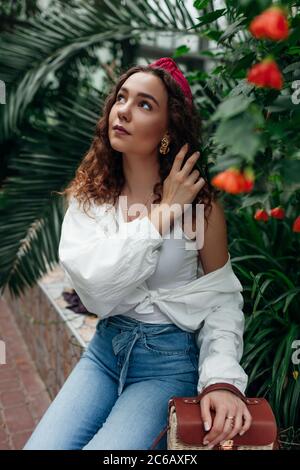 Hair hoop and purse. Young fashionable woman wearing stylish female accessories in garden among flowers. Stock Photo