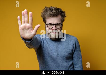 Serious man makes a stop gesture with hand and frowns at the camera. Stock Photo