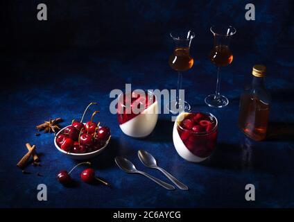 2 glass of panna cotta, traditional Italian dessert with poached cherries in rum and honey syrup, bowl of fresh cherries, 2 glass of rum. Low angle vi Stock Photo