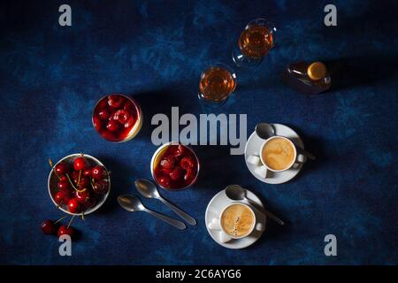 Panna cotta Italian traditional dessert with cherries poached in rum and honey syrup. Dark blue background table, bowl of the fresh cherries, 2 glass Stock Photo