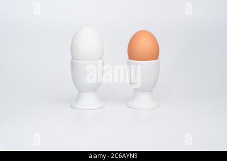 A white duck egg and a brown chicken egg in white egg cups on a white background Stock Photo