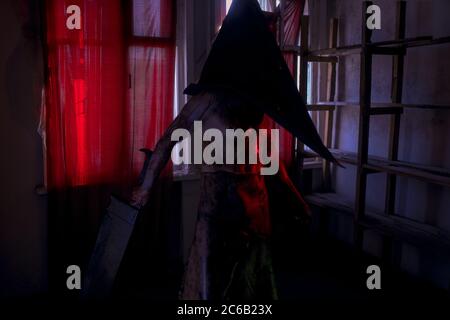 Cosplayer in the image of executioner stands in dark room with knife in his hand and helmet on his head. Stock Photo