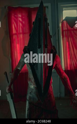 Cosplayer in the image of executioner stands in dark room with knife in his hand and helmet on his head. Stock Photo