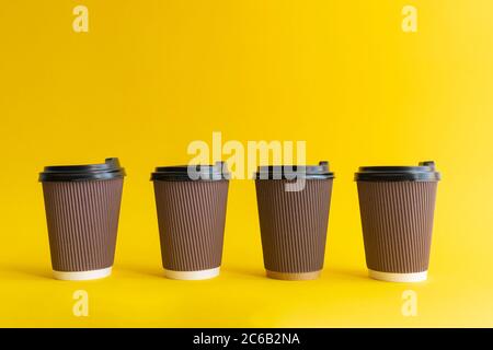 Four brown togo coffee paper cups with black covers on yellow background, Stock Photo