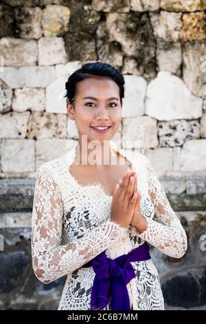 A young Balinese woman in a local temple dress making a formal greeting and smiling, Bali, Indonesia, Southeast Asia, Asia Stock Photo