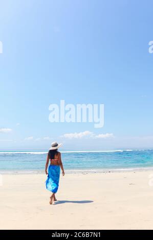 A young woman in a sunhat and shawl walking along a pristine tropical beach on Bali island, Indonesia, Southeast Asia, Asia Stock Photo