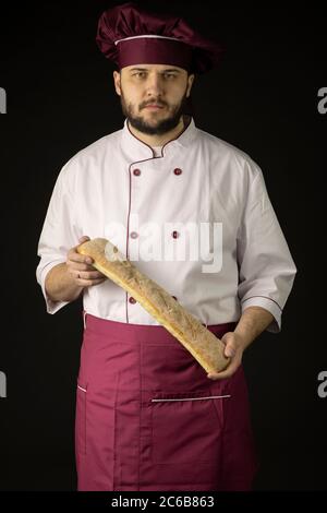 male baker man holding Baguette bread looking at camera isolated on black Stock Photo
