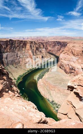 A vertical shot of a river flowing through green trees on a slope of a ...