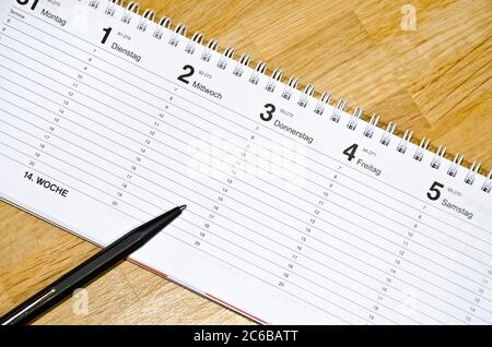 Pen lying on a schedule on a wooden desk (with captions of the days of the week in German) Stock Photo