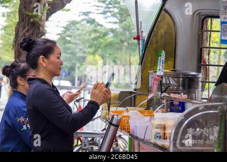 Shenzhen, China - November 14 2018: Two female customers use smartphone to pay their breakfast purchase at a street booth with Qr code payment. Digita Stock Photo