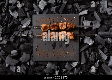 Kebab on skewers. Two portions of grilled meat on a stone plate. Charcoal background. Stock Photo