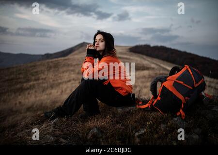 young woman hiker with a backpack sits on a rock and admires the incredible mountain scenery Stock Photo