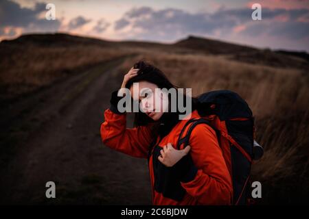 Portrait of a young tourist woman with a backpack straightening her long hair. Young beautiful woman traveling in the mountains Stock Photo
