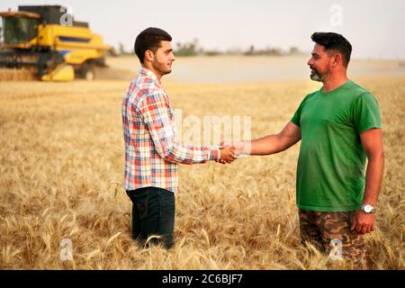Farmer and agronomist shaking hands in wheat field after agreement. Agriculture business contract concept. Corporate farmer and landlord rancher