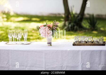 Bouquet of flowers and empty glasses on a table in a garden during a summer day before a toast. Stock Photo