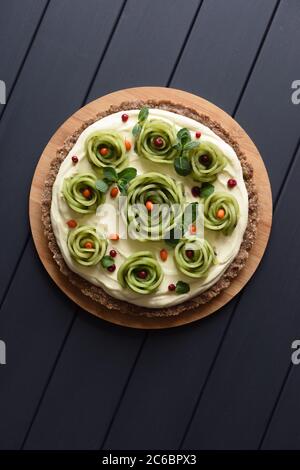 Raw vegan dessert. Homemade tart with rose shaped kiwi, berries, mint and cream filling on dark background top view copyspace Stock Photo