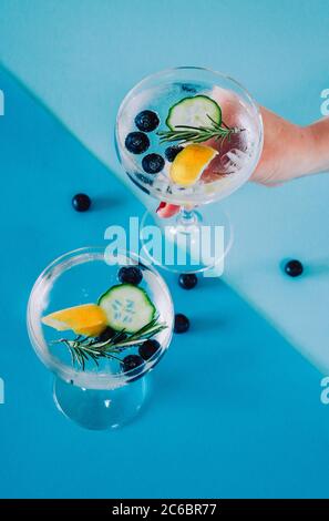 2 glasses of gin and tonic drink with blueberries, cucumber, rosemary   isolated on abstract, colourful, geometrical coloured background Stock Photo