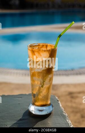Empty frappe glass with straw located at the side of a holiday swimming pool Stock Photo