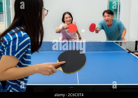 Couple fun playing table tennis or Ping pong indoor together leisure with competing in sports games at house. Father mother and daughter Asian family Stock Photo