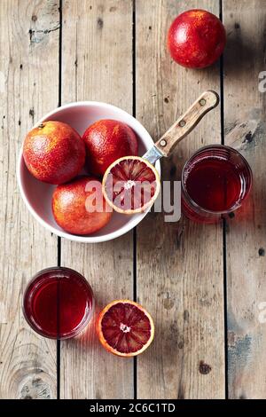 Red blood oranges in bowl and citrus drink on a wooden background, top view. Stock Photo