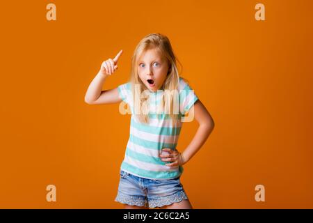 portrait of a happy blonde girl in a blue T-shirt on a yellow background. child's emotions, space for text Stock Photo