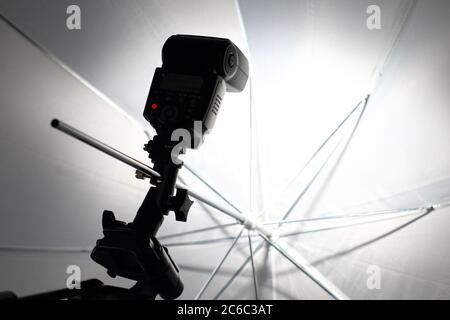 Camera flash flashes in a white umbrella in the photography studio. Stock Photo