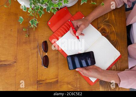 Woman hands writing on an orange agenda and holding cell phone Stock Photo
