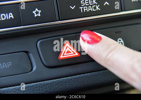 Woman pressing red triangle car hazard warning button. Female finger hitting car emergency light botton. Stock Photo