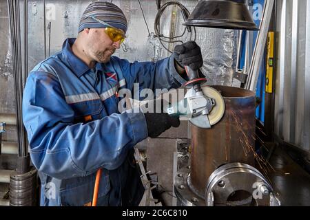 St. Petersburg, Russia - December 24, 2018: A locksmith uses manual pneumatic grinder to grind a steel part in metal factory. A worker uses safety gla Stock Photo