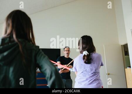 Man has a sword fight with toy sword and light saber with girls Stock Photo