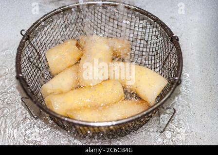 washing cassava with water in a metal strainer, Manihot esculenta. Cassava, also called mandioca, yuca, balinghoy, mogo, mandioca, kamoteng kahoy, tap Stock Photo