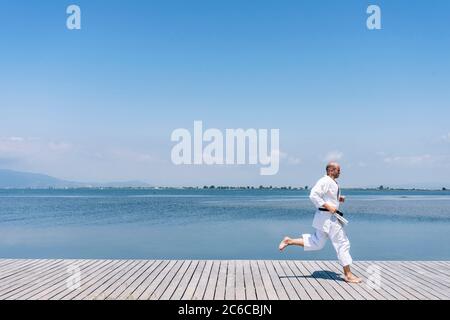 A man practices martial arts running on a wooden walkway by the sea Stock Photo