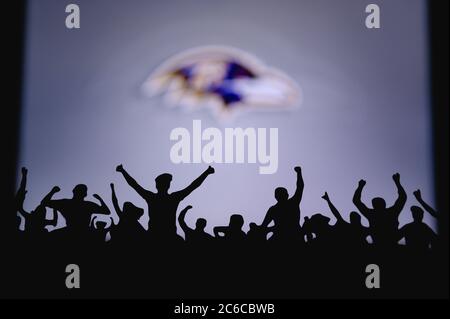 Baltimore Ravens. Fans support professional team of American National Foorball League. Silhouette of supporters in foreground. Logo on the big screen. Stock Photo