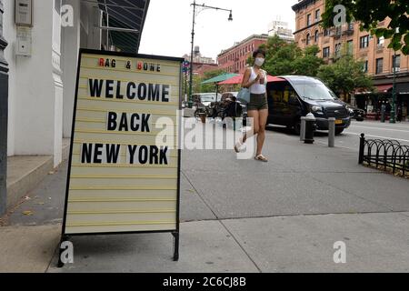 New York City, USA. 08th July, 2020. A woman wearing a mask in the time of COVID-19 walks along Columbus Ave. where a sign sits outside Rag and Bone fashion retailer welcoming New Yorkers back to shop as New York City moves into Phase 3 of reopening, in New York, NY, July 8, 2020. (Anthony Behar/Sipa USA) Credit: Sipa USA/Alamy Live News Stock Photo
