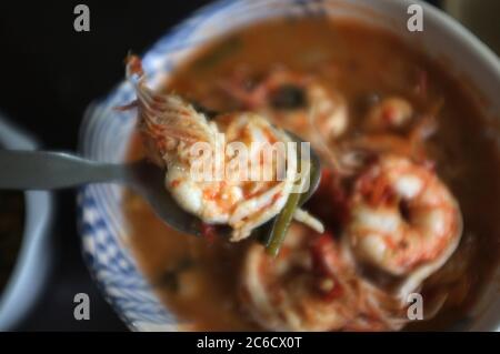 Close up Woman hand hold a spoon with shrimp from Tom Yum Goong Spicy Sour Soup or River prawn spicy soup on wood table . Thai food Stock Photo