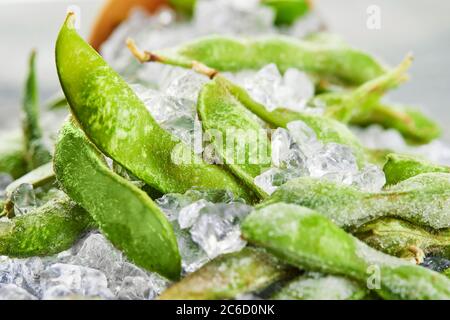 Frozen Edamame or soybeans in the mix with crushed ice on a blue background. Stock Photo