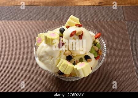 side view bowl of vanilla flavor ice cream sundae starts melting with marshmallows and various nuts Stock Photo