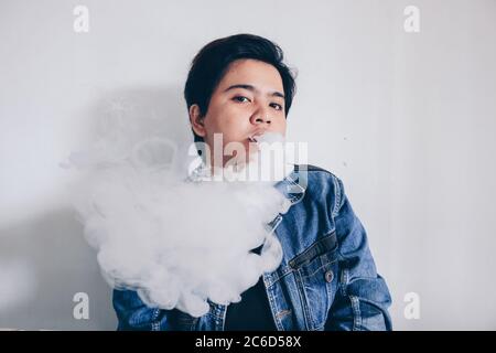 Asian beautiful short hair girl wear jeans jacket is smoking electronic cigarette or vaping vape on white background Stock Photo