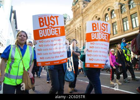 Protesters carry ‘Bust the Budget’ placards against cuts to health, welfare, education, foreign aid and the ABC as they march along George Street past Stock Photo