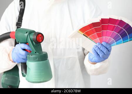 Man holds in his hands spray gun and palette of colors. Stock Photo